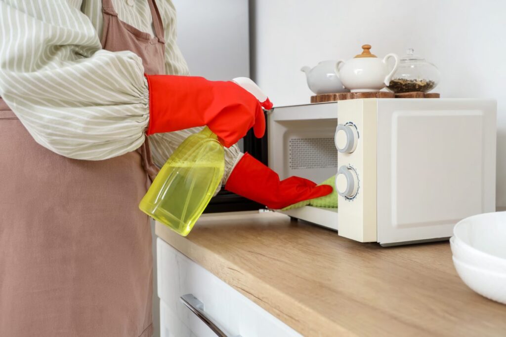 Osoba w gumowych rękawicach spryskująca wnętrze mikrofalówki środkiem czyszczącym