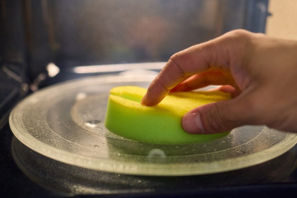 Ręka z gąbką czyszcząca szklany talerz wewnątrz mikrofalówki