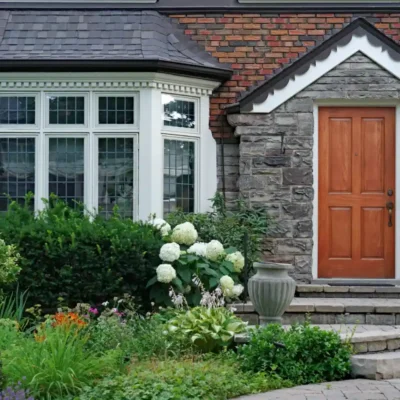 jak urządzić ogród przed wejściem do domu grafika główna przedstawiająca angielski dom z bujnym zielonym przedogródkiem