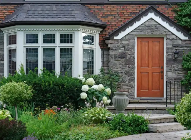 jak urządzić ogród przed wejściem do domu grafika główna przedstawiająca angielski dom z bujnym zielonym przedogródkiem