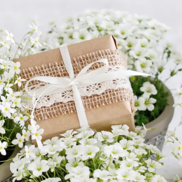 ozdobny prezent na komunię umieszczony wśród białych kwiatów