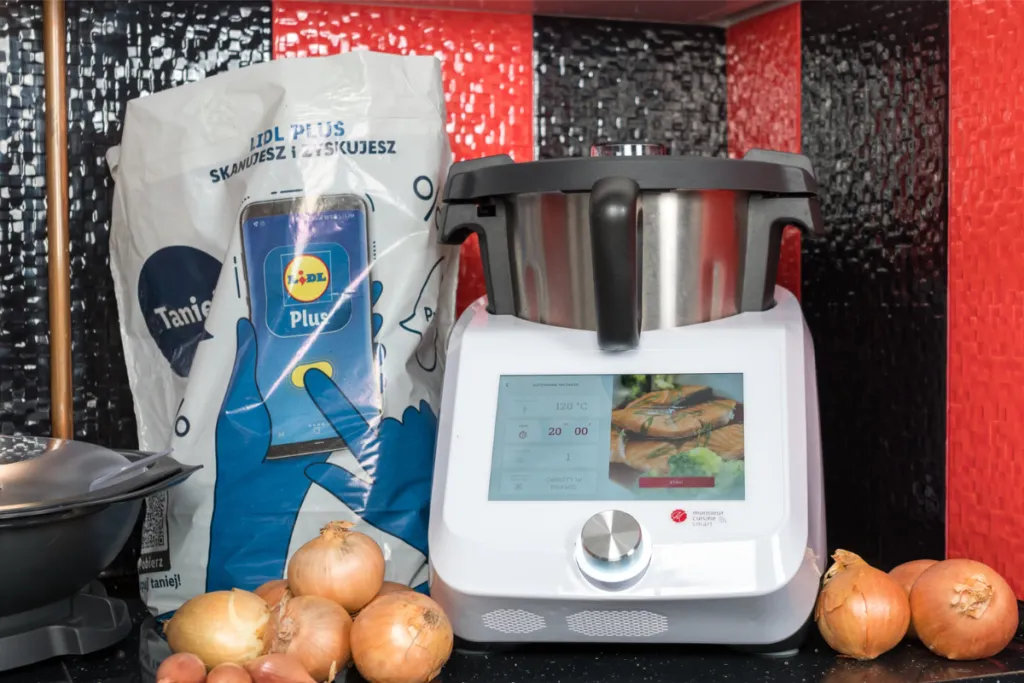 Monsieur Cuisine z wyświetlaczem pokazującym przepis, otoczony cebulami i torbą z Lidla