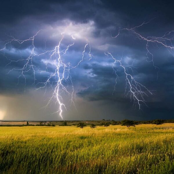 Rozległe pole pod burzowym niebem z wieloma błyskawicami – widoczna linia horyzontu i nadciągająca nawałnica