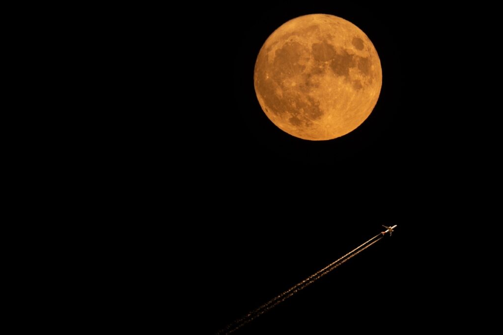 Samolot przelatujący na tle pomarańczowego superksiężyca podczas sierpniowej pełni