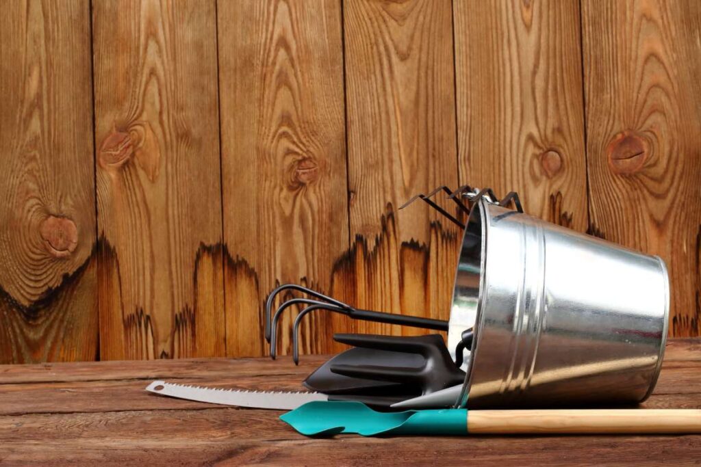 Metalowe wiaderko z narzędziami ogrodniczymi na drewnianym stole przy drewnianym płocie