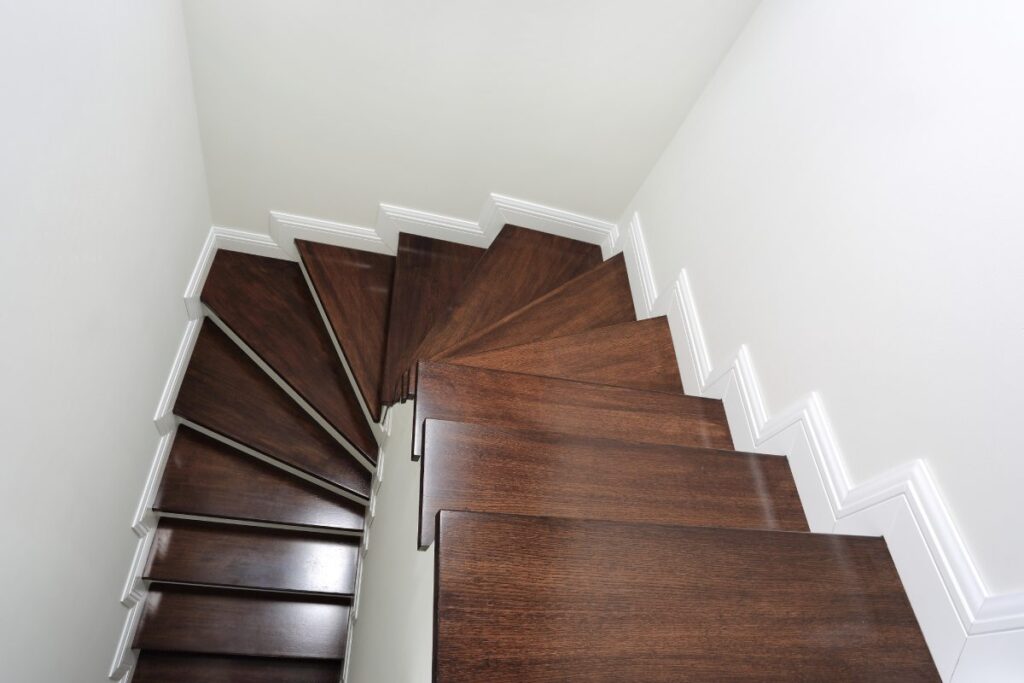 Ciemnobrązowe panele wykończone na schodach w nowoczesnym wnętrzu z białymi ścianami i listwami przypodłogowymi.