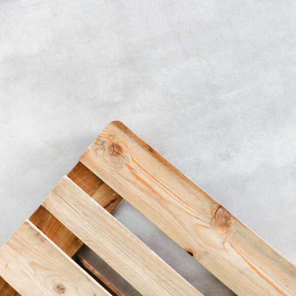 Fragment drewnianej palety na tle jasnej, betonowej powierzchni.