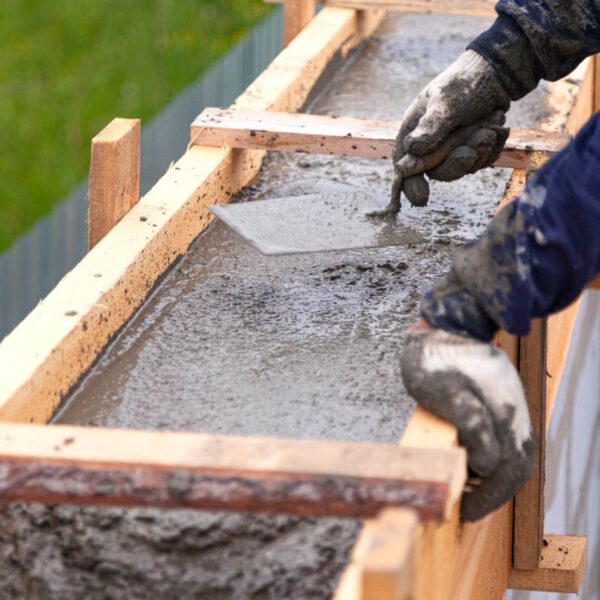 Ręczne wygładzanie świeżo wylanego betonu w drewnianym szalunku podczas budowy schodów.
