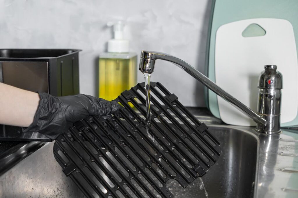 Mycie wyjmowanego kosza z frytkownicy beztłuszczowej pod bieżącą wodą w zlewie.