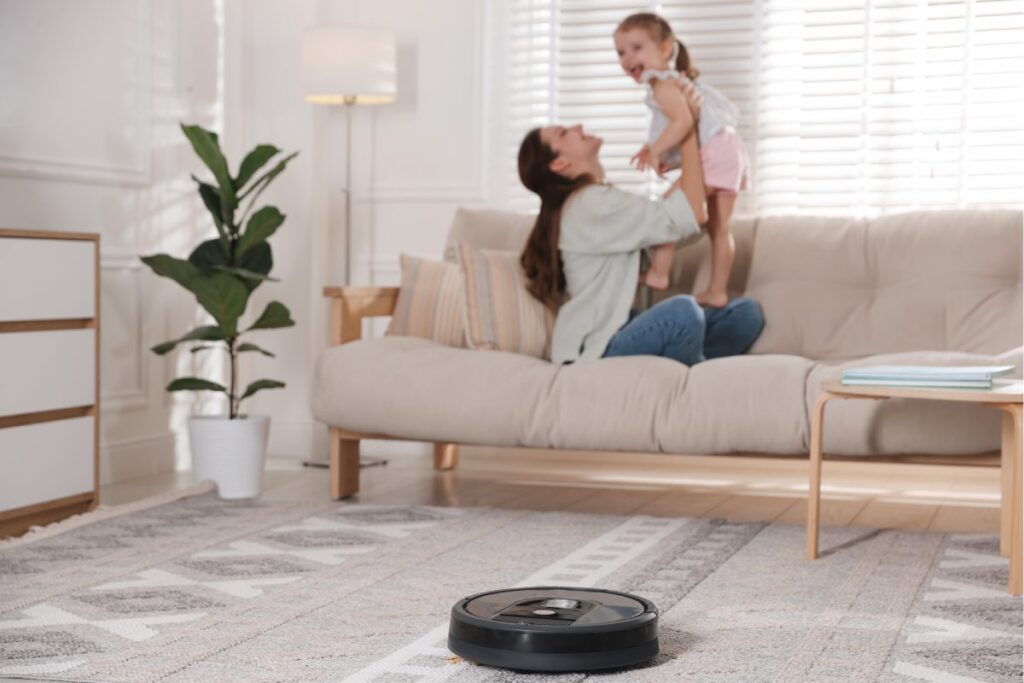Kobieta z dzieckiem na sofie, w tle pracuje robot sprzątający