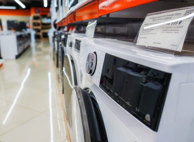 Rząd pralek ustawionych w sklepie z AGD, widok z boku, półka z cenami.