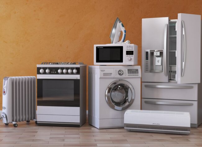 Domowe sprzęty AGD ustawione przy ścianie – piekarnik, pralka, mikrofalówka, lodówka, grzejnik, klimatyzator – przykładowe wyposażenie kuchni i pralni.