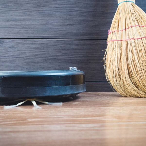Robot sprzątający obok tradycyjnej miotły na drewnianej podłodze w nowoczesnym wnętrzu