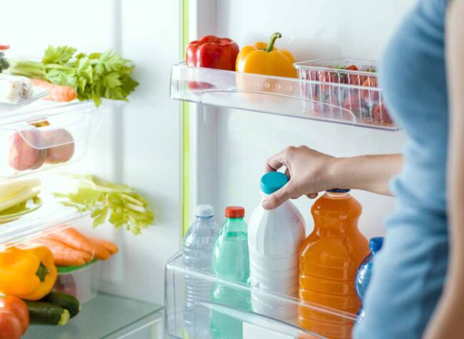 ręka wkładająca napoje do półki w lodówce