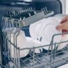 Mała zmywarka z wysuniętym koszem i białymi talerzami w środku