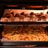 Piekarnik z dwoma poziomami pieczenia, na których pieką się kurczak i frytki