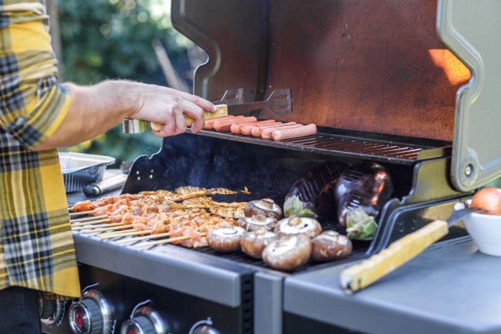 Grill gazowy z otwartą pokrywą podczas przygotowywania kiełbasek, szaszłyków i warzyw