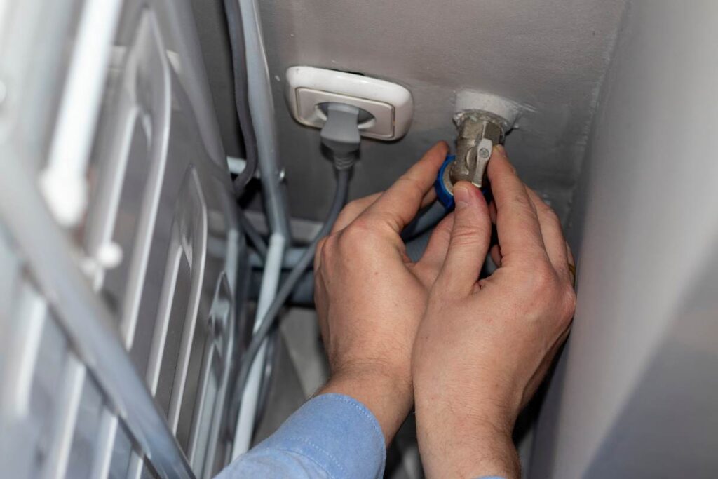 Podłączanie pralki do zaworu wody i gniazdka elektrycznego – zbliżenie na instalację za urządzeniem