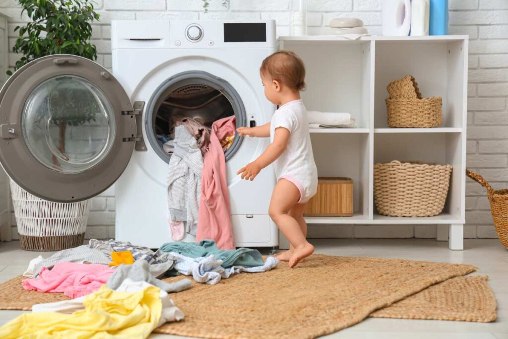 Dziecko wyciąga kolorowe ubranka z otwartej pralki w domowej pralni