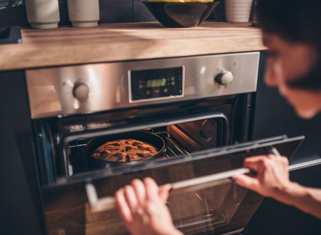 Osoba otwierająca piekarnik elektryczny z upieczonym ciastem w środku