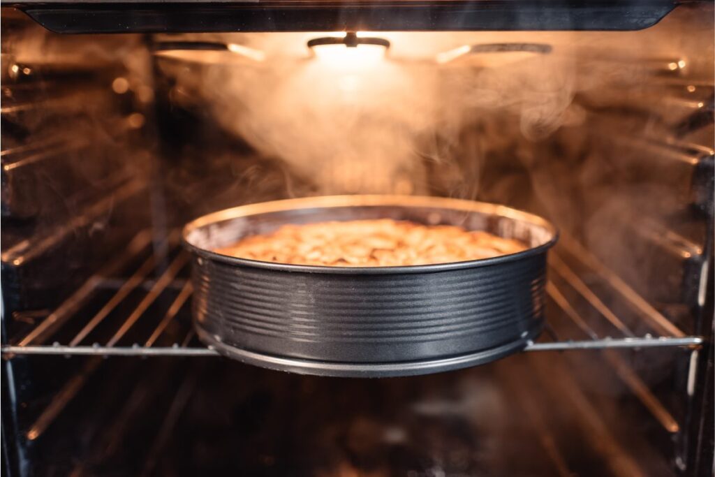 Ciasto pieczone w okrągłej formie we wnętrzu piekarnika z widoczną parą wodną
